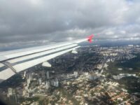 Pessoa escolhendo roupa confortável para viajar de avião, com malas ao fundo.