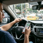 Motorista segurando celular ao volante, com foco em multa de trânsito.