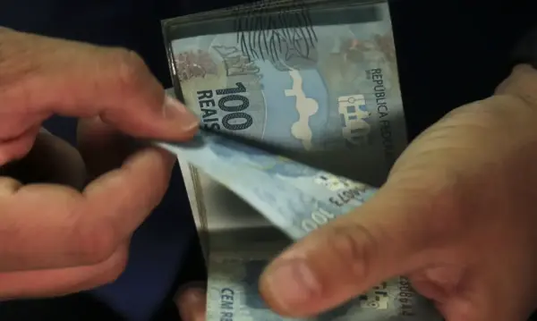 Pessoa olhando para carteira vazia com gráfico de custo de vida subindo ao fundo.