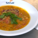 Prato de caldo de canjiquinha com costela defumada servido em tigela, com cheiro-verde picado por cima.