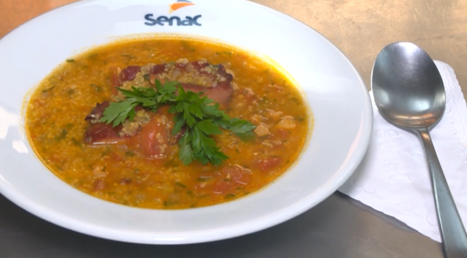 Prato de caldo de canjiquinha com costela defumada servido em tigela, com cheiro-verde picado por cima.